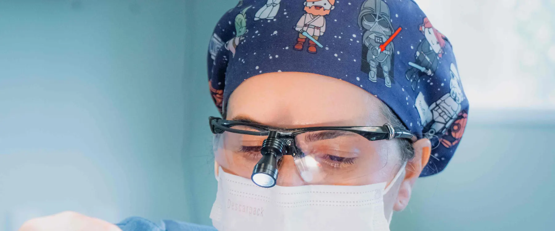 Dra. Xenia Tavares em cirurgia, com touca, lupa cirúrgica e máscara